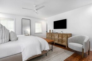 Un dormitorio con cama, una silla, un televisor, un tocador y un ventilador de techo.