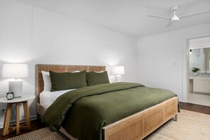 Ein ordentlich eingerichtetes Schlafzimmer mit einem Bett, Nachttischlampen, einem kleinen Tisch und einem Deckenventilator.