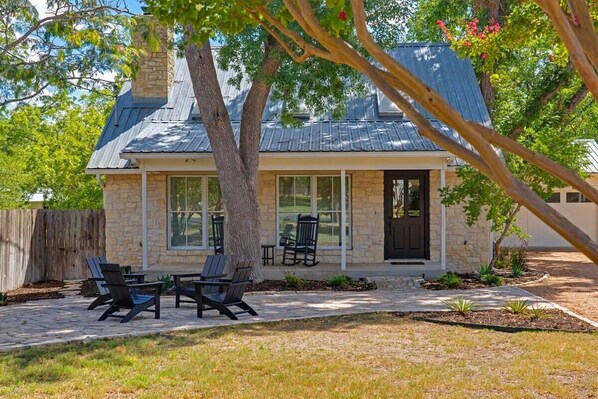 Une maison en pierre avec un patio couvert, un espace salon extérieur et un grand arbre au premier plan.