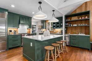 A modern kitchen with green cabinets, a central island with stools, and pendant lighting. - Fab-Fred House, Patio Oasis, Fireplace, In Town (Fredericksburg)