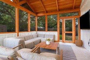 A covered patio with a sectional sofa, a wooden table, and a television.