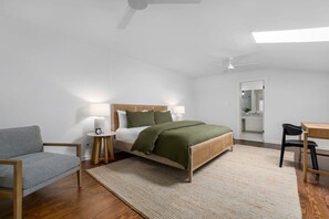 Ein Schlafzimmer mit Bett, Nachttischen, einem Sessel, einem Schreibtisch und einem Deckenventilator.