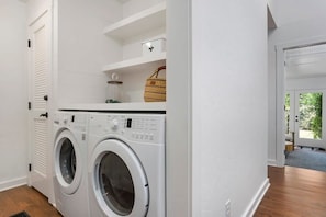 A laundry room with two front-loading washing machines, a white tiled wall, and a basket on a shelf.