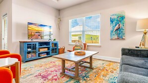 A room with a large window, a blue cabinet, a table with a woven basket, and a gray sofa. - Bay View Retreat | Heated Pool | Dog Friendly | Near Beaches (Port St Joe)