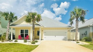 A single-story house with a garage, a covered porch with two red chairs, and a well-maintained lawn. - Bay View Retreat | Heated Pool | Dog Friendly | Near Beaches (Port St Joe)