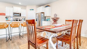 A modern kitchen with white cabinets, a wooden dining table, and orange chairs. - Bay View Retreat | Heated Pool | Dog Friendly | Near Beaches (Port St Joe)