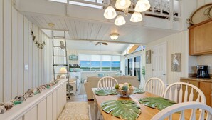 A dining area with a wooden table, white chairs, and a view of the ocean.
