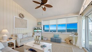 A living room with a large window, a ceiling fan, and a TV.