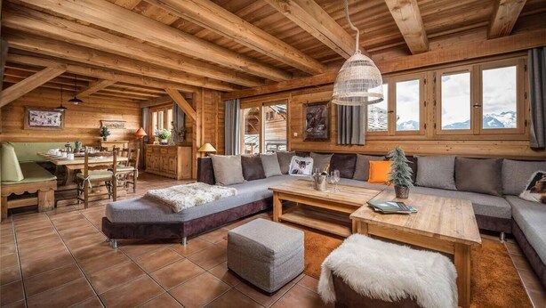 Ein gemütliches Blockhaus-Interieur mit Essbereich aus Holz, einer großen Couch und Blick auf Berge durch die Fenster.