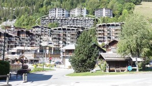 A multi-story hotel with balconies, situated in a mountainous area with a view of the forest. - OURS BLANC 9 – Studio with a beautiful mountain view, close to the aquatic area. (La Clusaz)