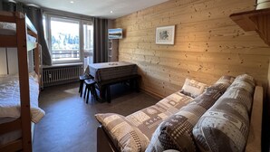 A cozy room with a wooden wall, a sofa, a table, and a bunk bed. - OURS BLANC 9 – Studio with a beautiful mountain view, close to the aquatic area. (La Clusaz)