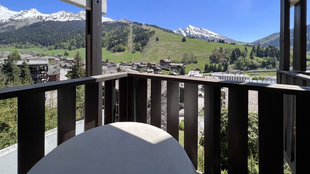 A balcony with a view of a mountainous landscape, including snow-capped peaks and a village below. - OURS BLANC 9 – Studio with a beautiful mountain view, close to the aquatic area. (La Clusaz)