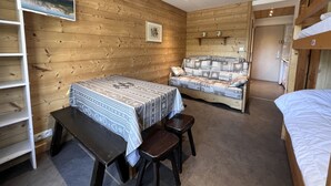 A cozy room with wooden walls, a bed, a sofa, a desk, and a picture of a mountain landscape. - OURS BLANC 9 – Studio with a beautiful mountain view, close to the aquatic area. (La Clusaz)