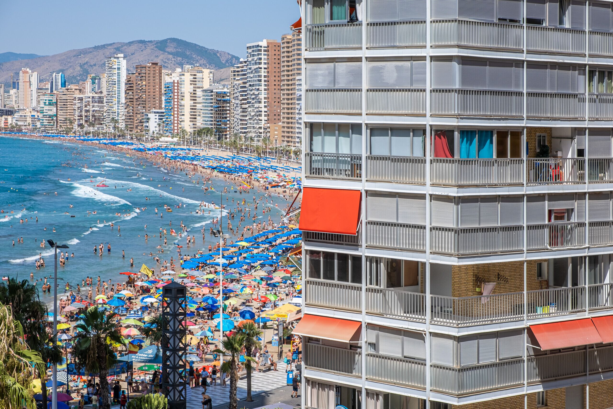 Un hôtel situé sur la côte, doté de nombreux balcons, offrant une vue sur la plage et donnant sur une plage très fréquentée.