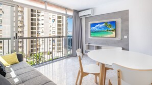 Un salon moderne avec balcon, un coin repas et un grand téléviseur fixé au mur.