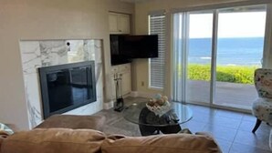 Sala de estar con sofá, televisor montado en la pared y vista al océano a través de puertas correderas grandes.