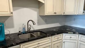 Una cocina con gabinetes blancos, encimera negra y pileta de acero inoxidable.