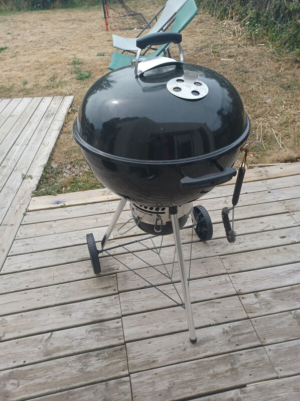 Ein schwarzer Grill mit Rädern auf einer Holzterrasse.