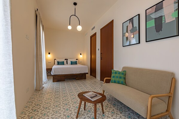 A hotel room with a bed, a sofa, a small table, and two paintings on the wall. - Luxury house in the old town with pool and close to the beach (Tarifa)