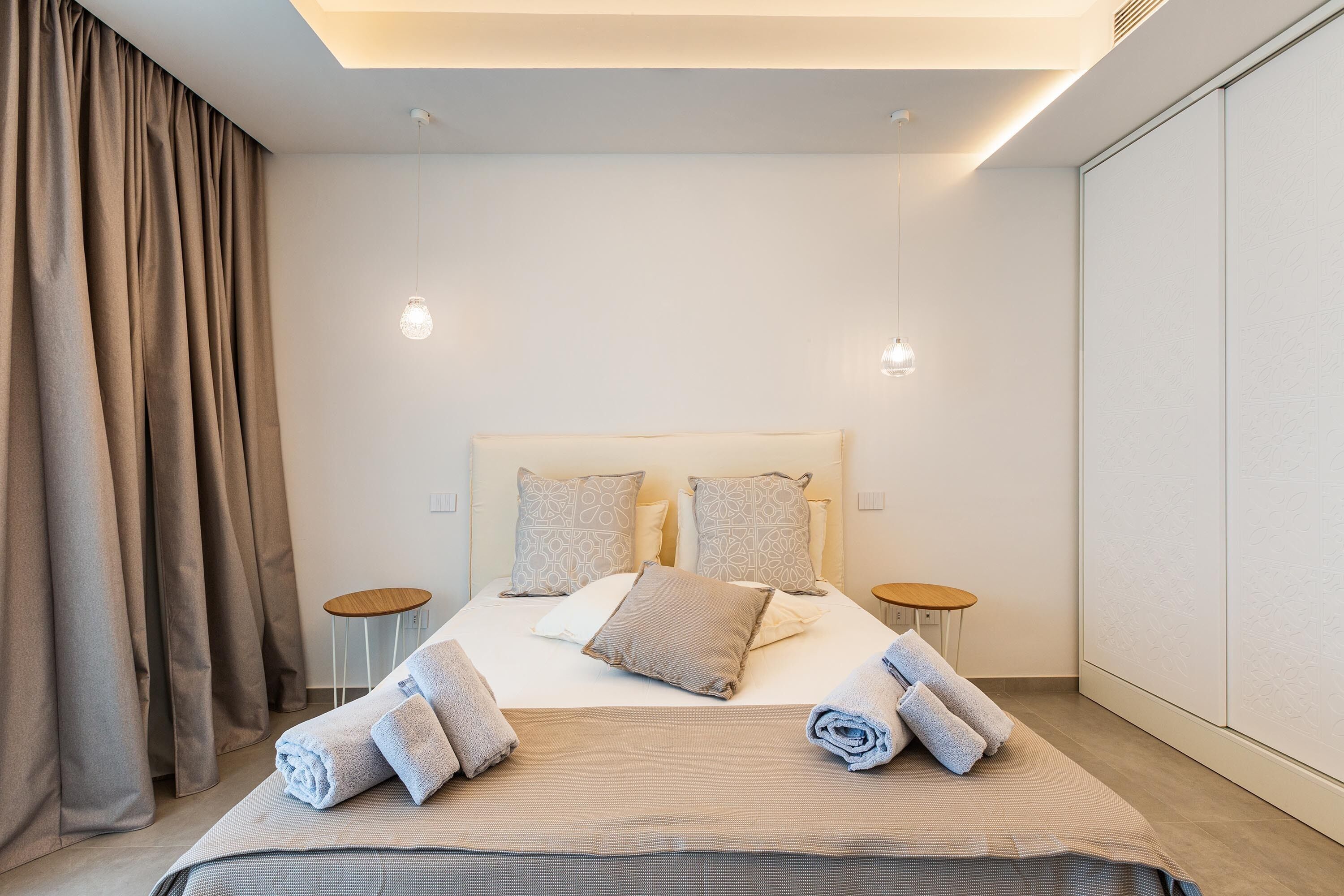 A modern hotel room with a large bed, two bedside tables, and a wardrobe.