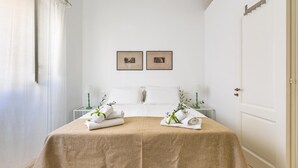En snyggt bäddad säng med ett beige överkast, två inramade tavlor på väggen och en vit dörr.