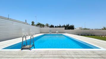Ein rechteckiger Pool mit Holzterrasse, zwei Liegestühlen und einer Leiter.