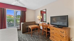 A hotel room with a bed, a desk with a chair, a television, a ceiling fan, and a window with curtains. - Metro Scottsdale Extended Stay (Paradise Valley)
