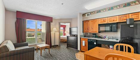 A compact hotel room with a kitchenette, a sofa, a dining table, and a TV.