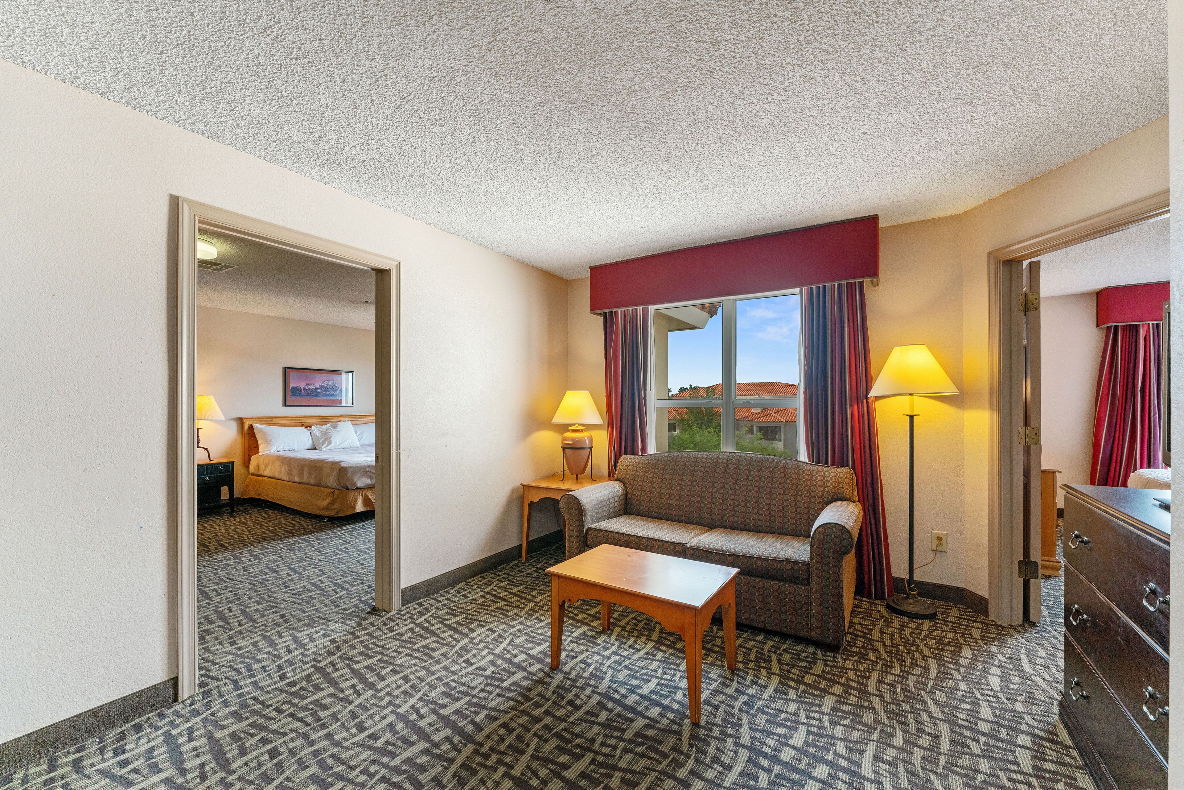 Una habitación de hotel con una cama, un sofá, una mesita, un aparador y dos lámparas.