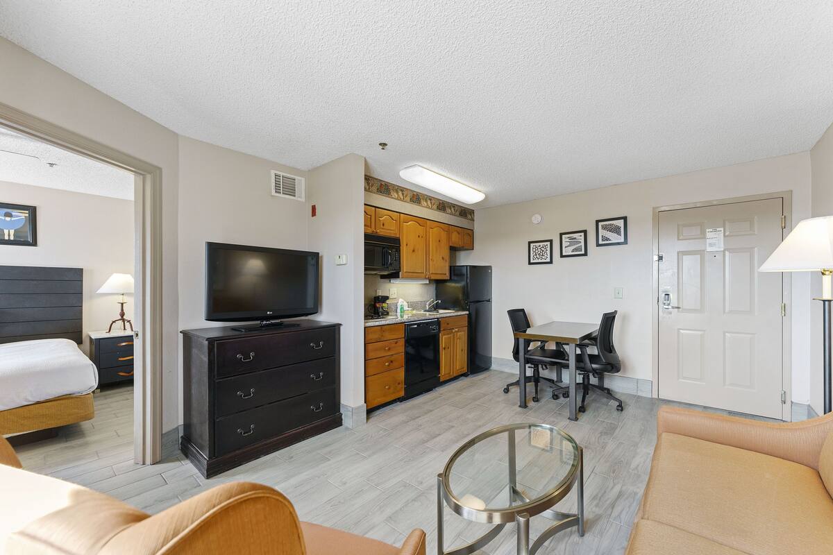 A compact hotel room with a bed, a TV, a kitchenette, and a dining area.