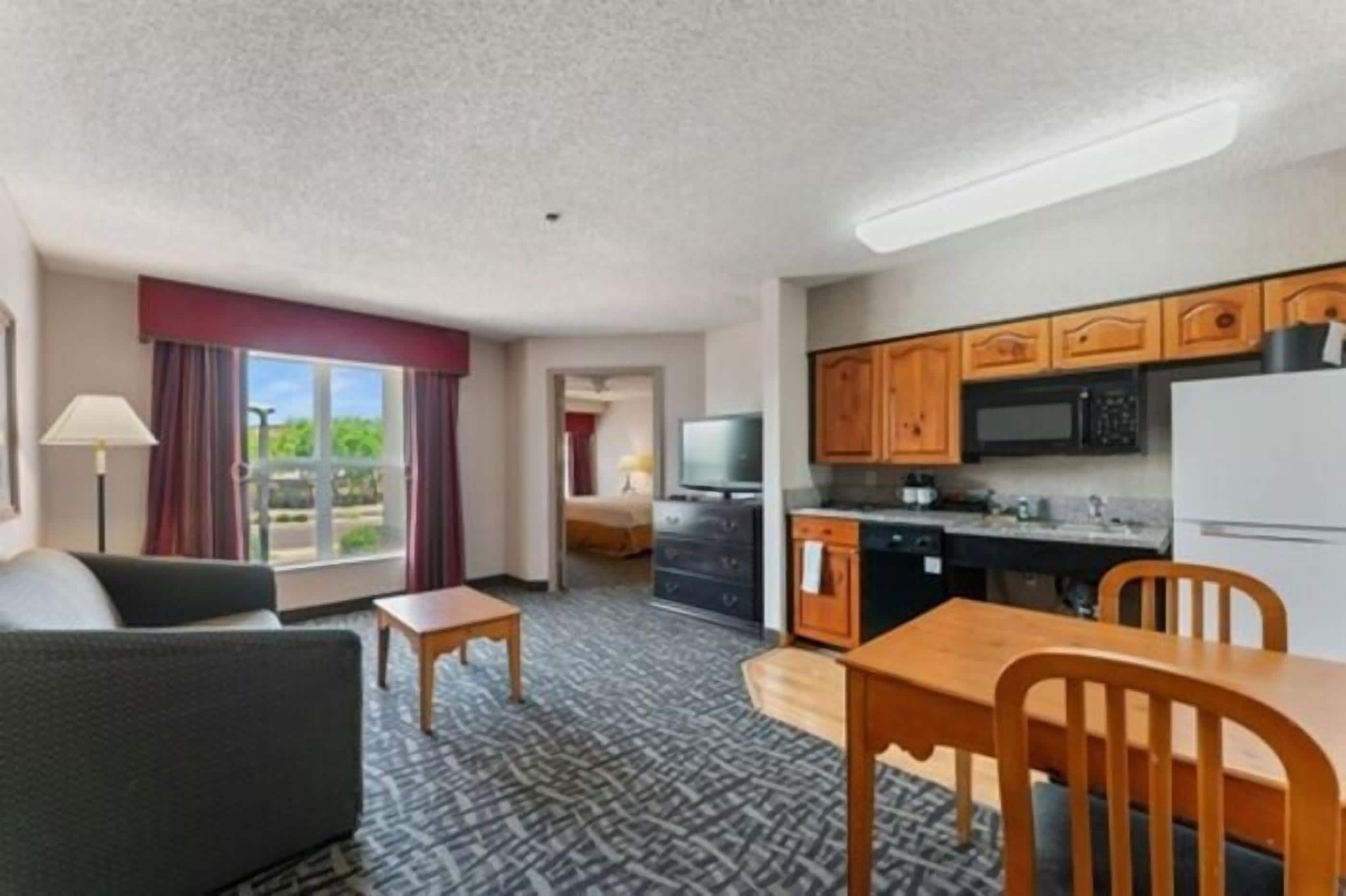 Habitación de hotel con sofá, una mesita, una mesa de comedor con sillas y una cocina con microondas, estufa y refrigerador.