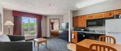 Habitación de hotel con sofá, una mesita, una mesa de comedor con sillas y una cocina con microondas, estufa y refrigerador.