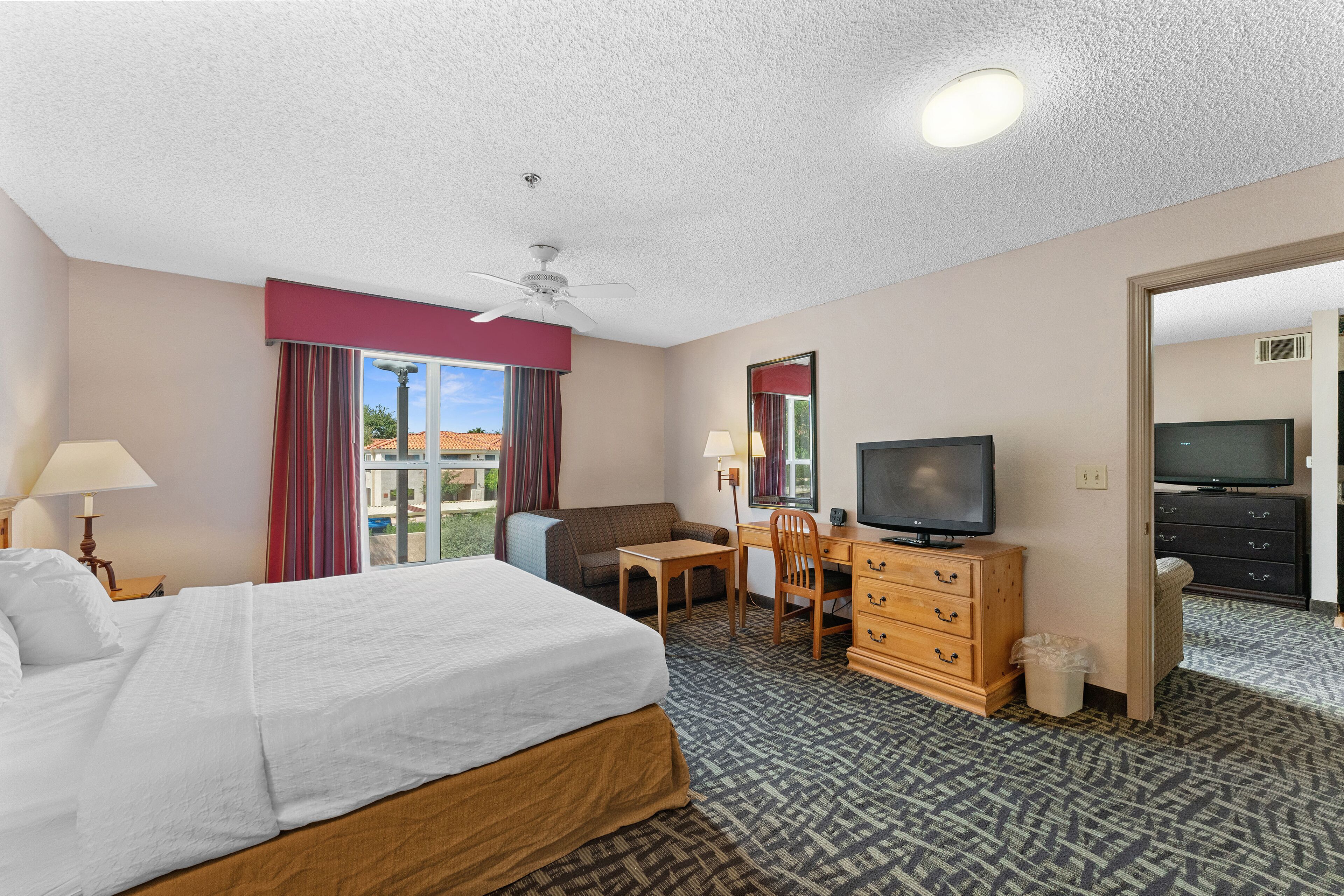 A hotel room with a bed, desk, TV, and a view of the outdoors.