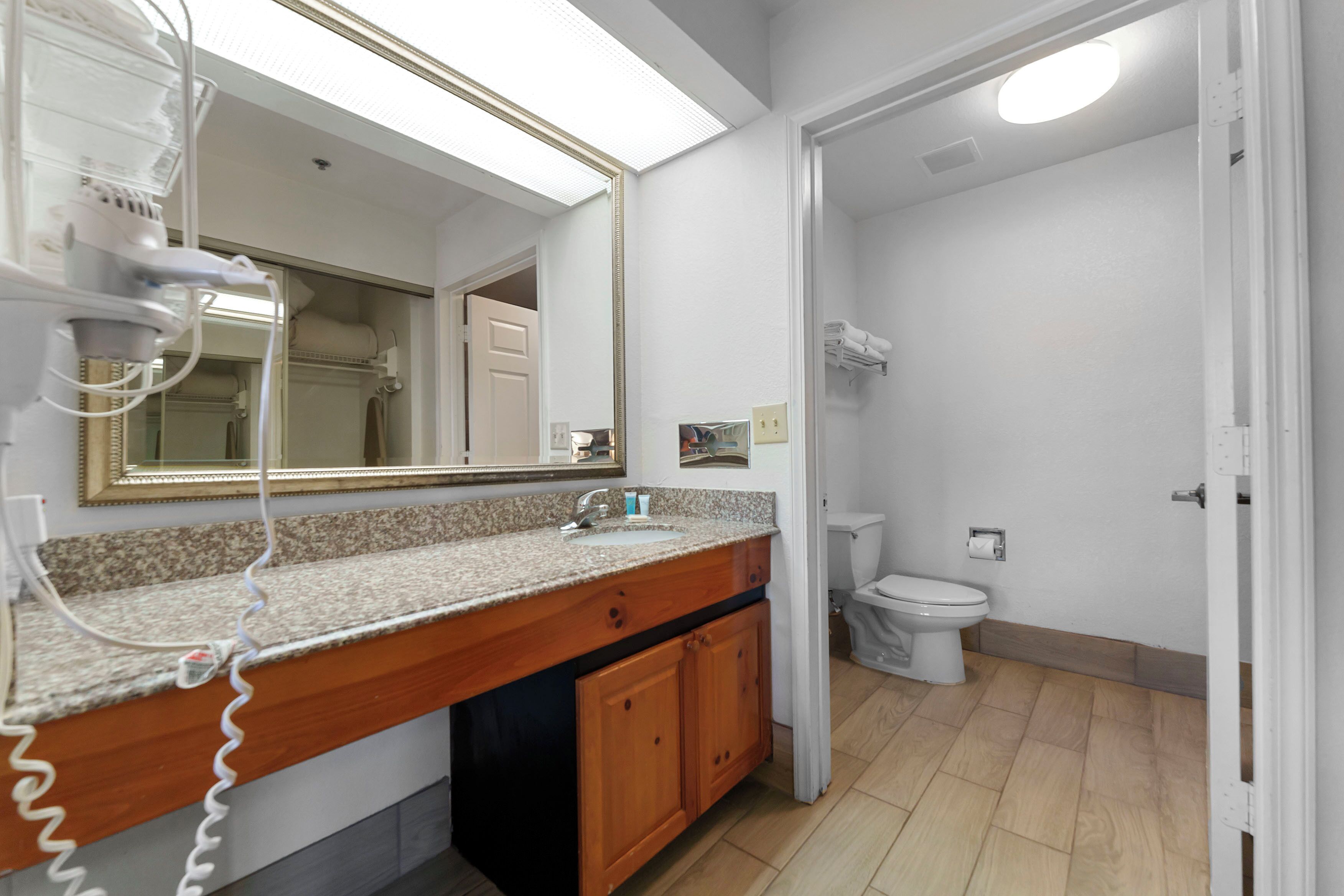 Un baño con encimera de granito, armarios de madera, inodoro blanco y zona de ducha.