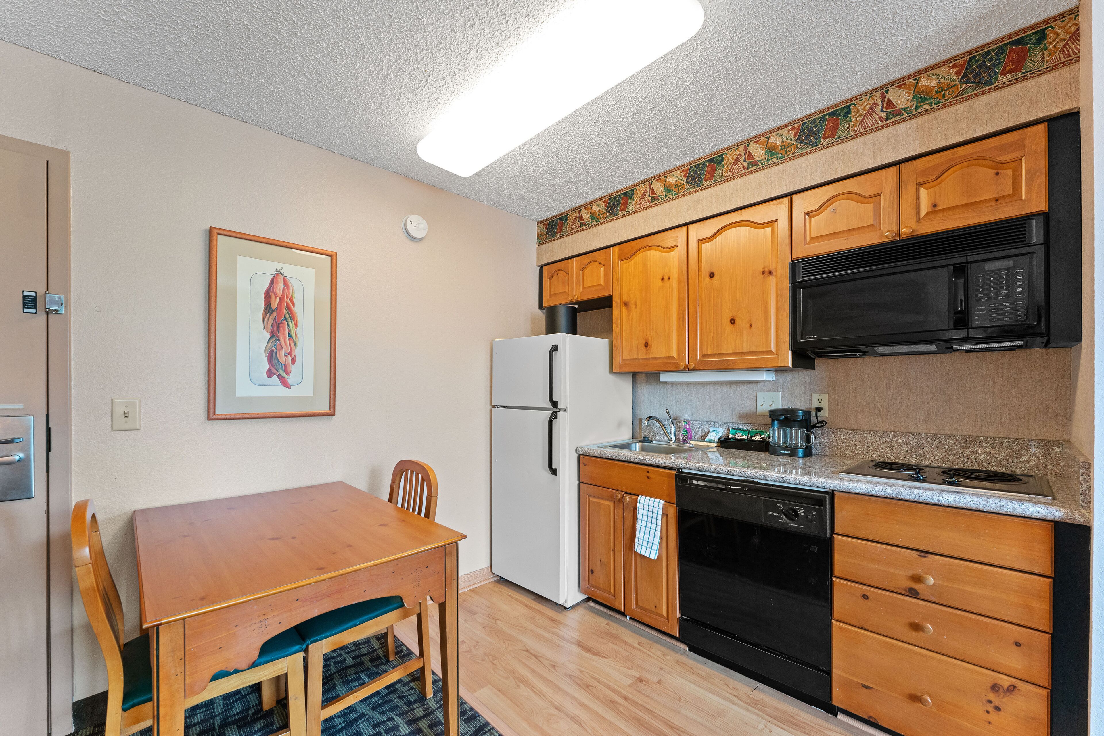A compact kitchen with wooden cabinets, a white refrigerator, a black microwave, and a stove.