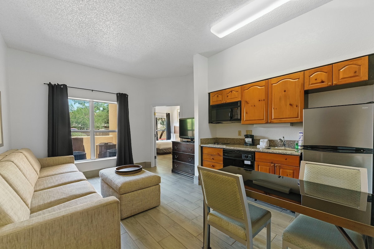 A modern apartment with a living room, kitchenette, and a view of the outdoors.