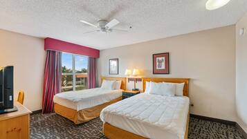 A hotel room with two beds, a ceiling fan, a TV, and a window with curtains.