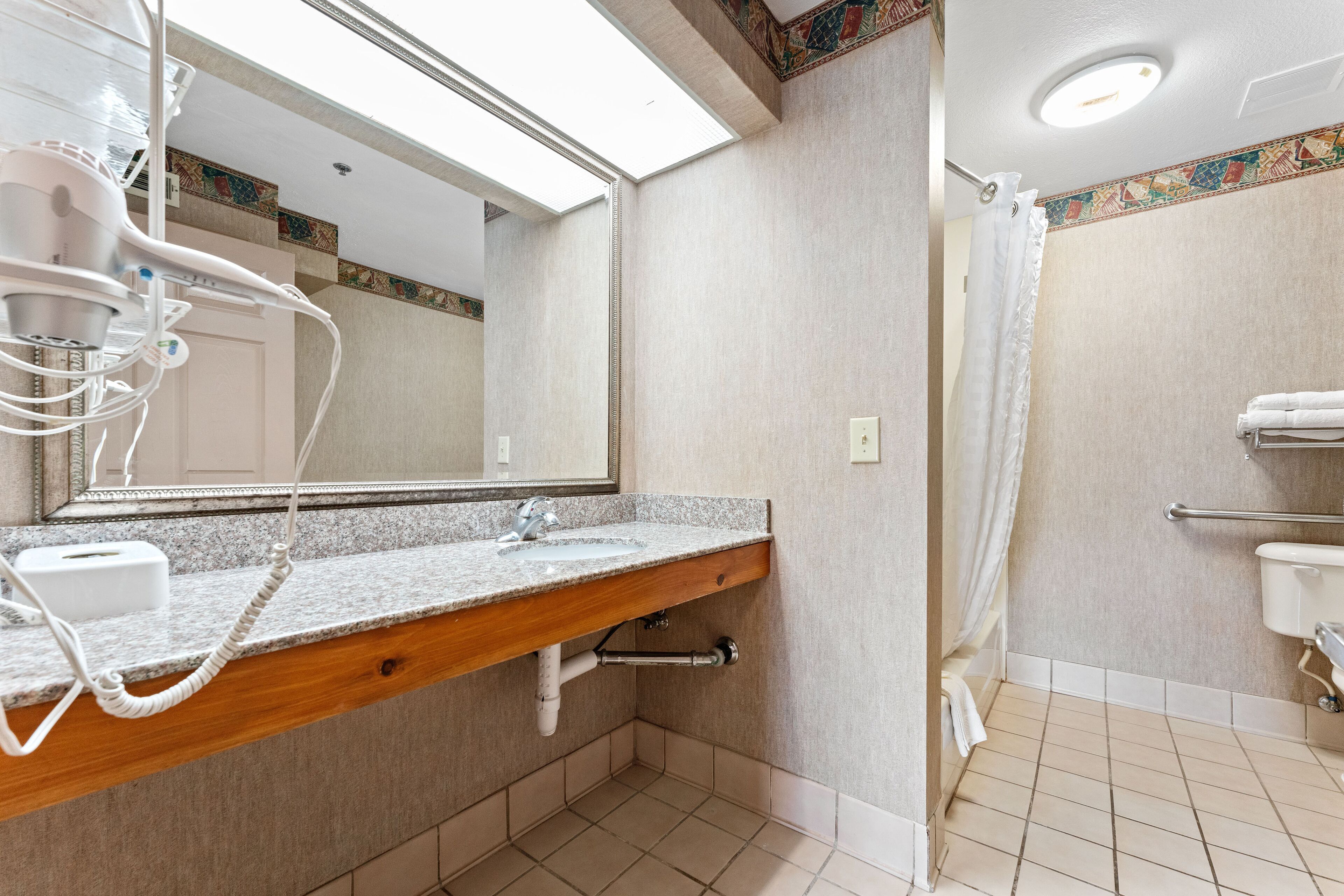 A bathroom with a granite countertop sink, a mirror, a shower curtain, and a towel rack.
