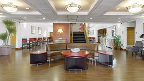 A spacious lobby with a curved brown leather sofa, two round tables, and a staircase leading to an upper level. - Metro Scottsdale Extended Stay (Paradise Valley)