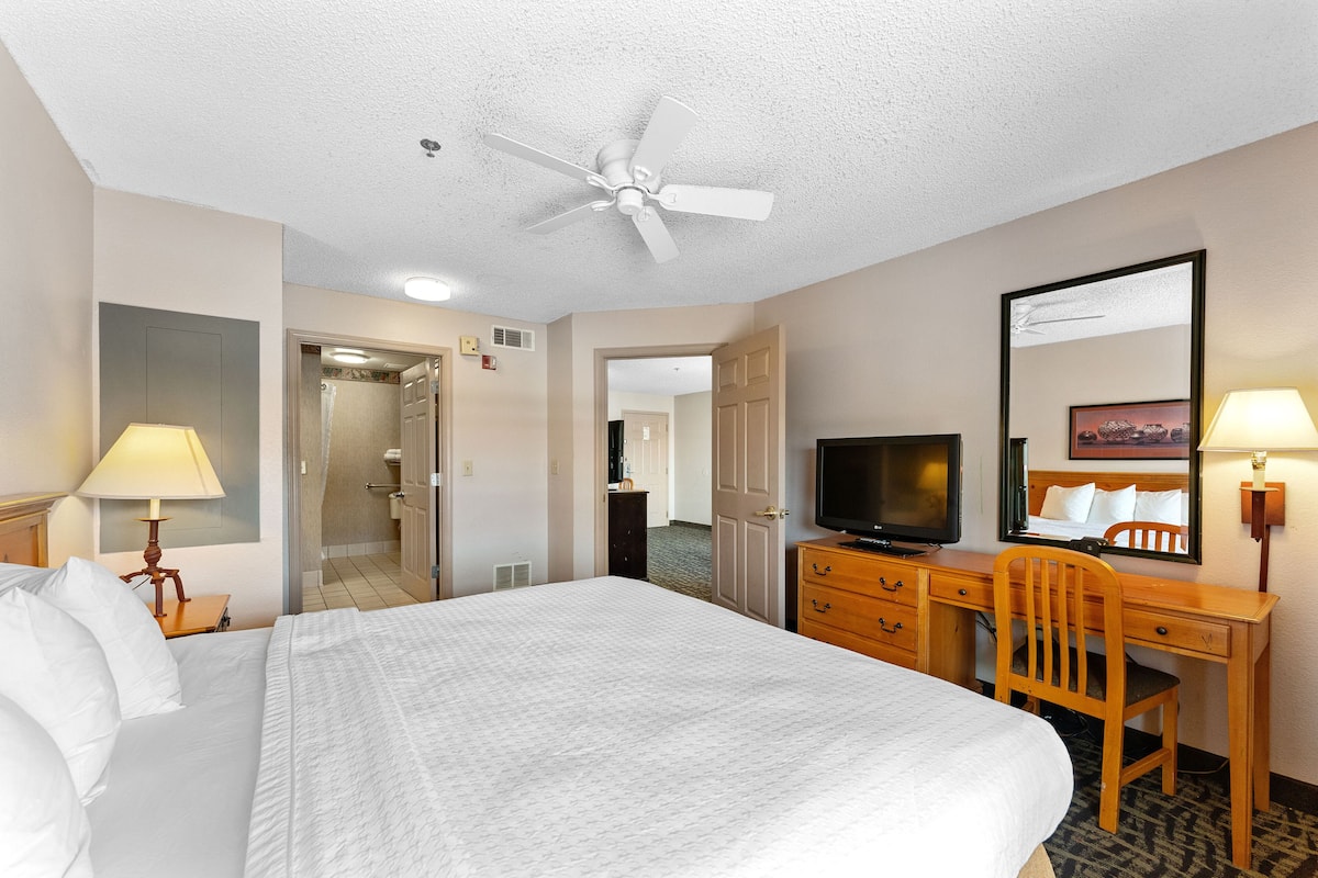 A hotel room with a bed, desk, chair, television, and a ceiling fan.