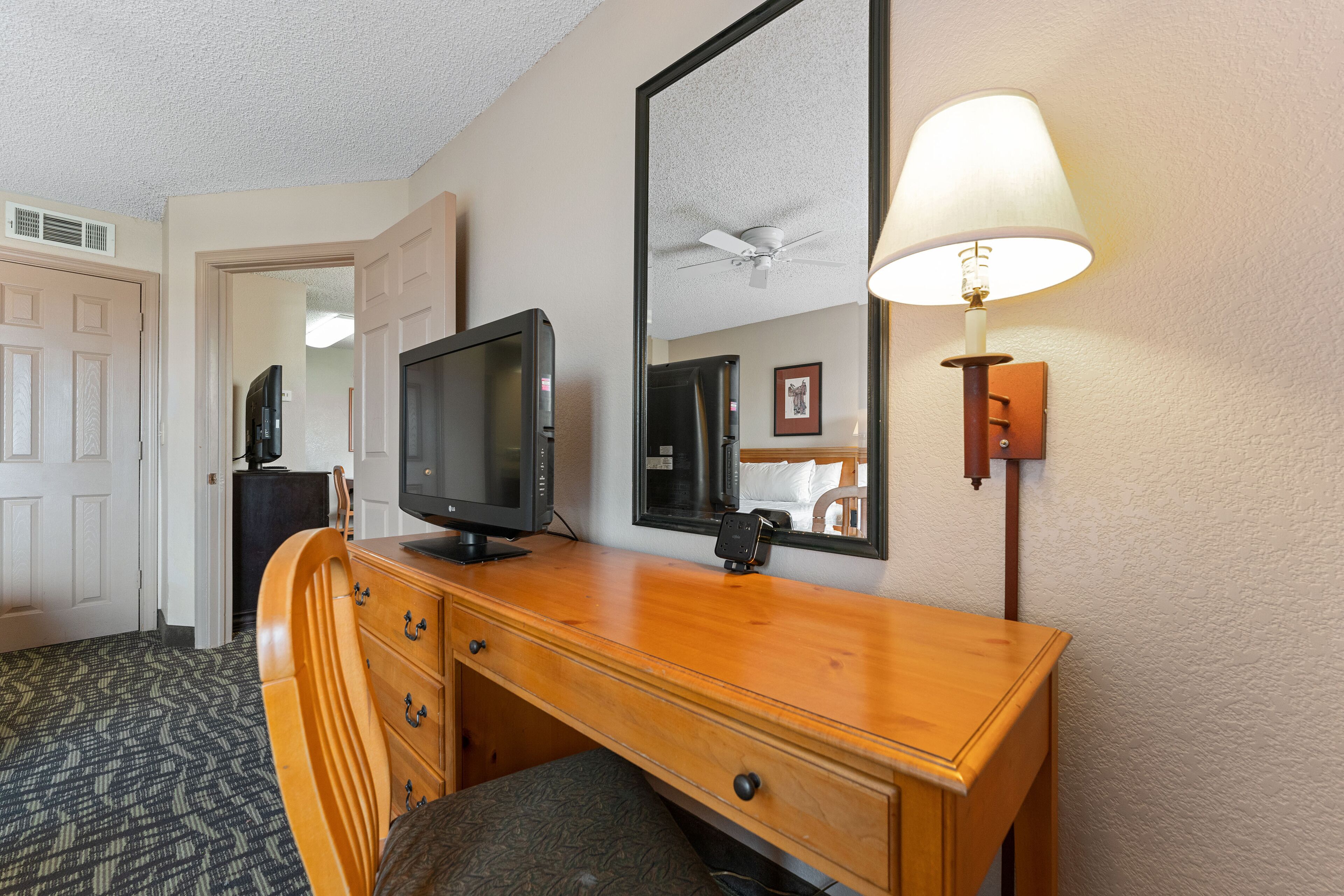 Una habitación de hotel con un escritorio de madera, televisor, espejo y lámpara.