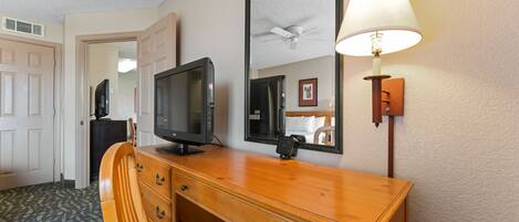 Una habitación de hotel con un escritorio de madera, televisor, espejo y lámpara.