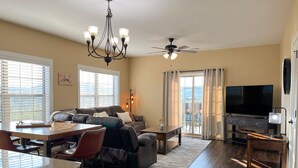A spacious living area with a dark wood floor, a large sofa, a dining table with chairs, a TV, and a ceiling fan. - Eagle's View - No Stairs - Minutes to SDC (Branson)