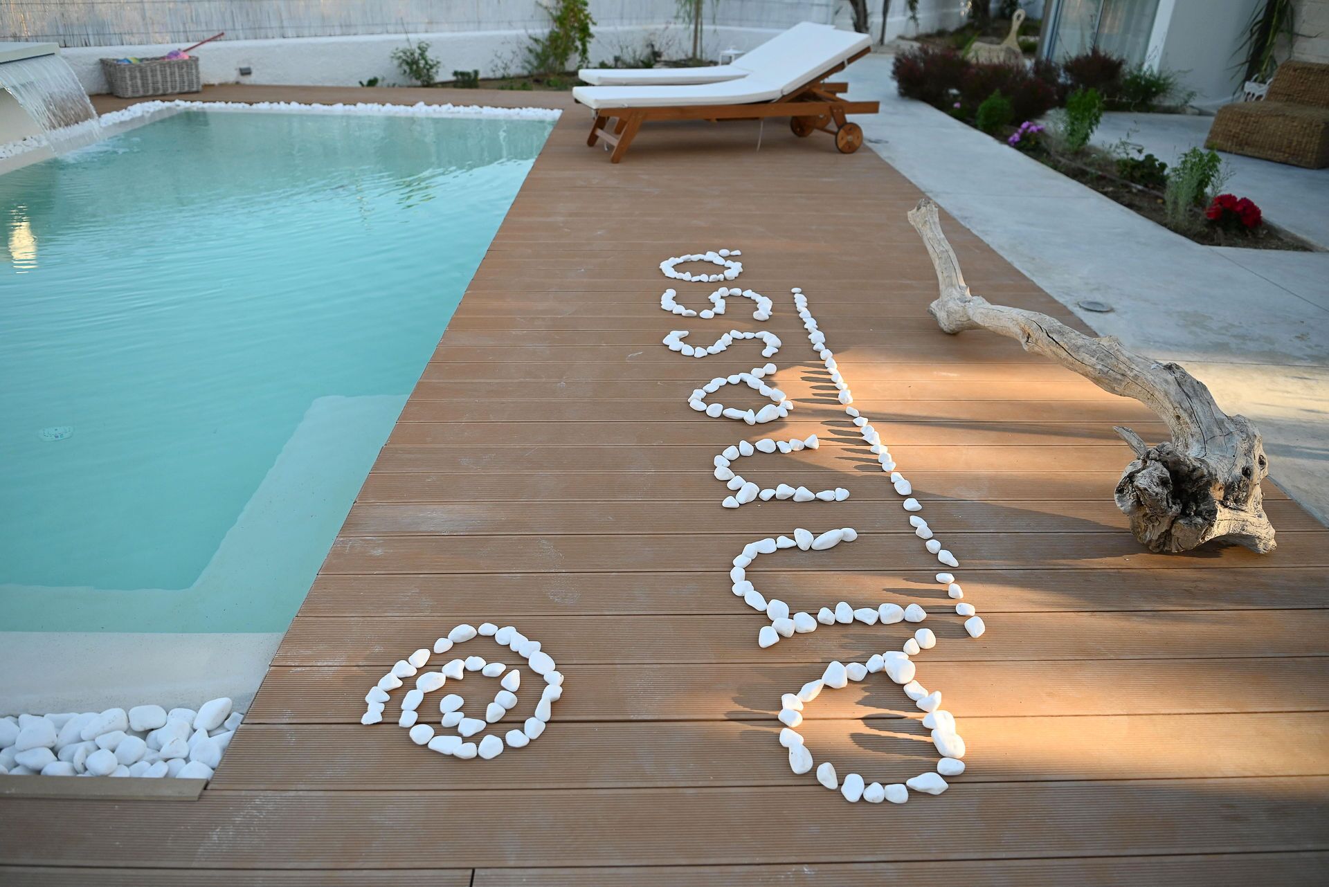 A wooden deck with a pool, lounge chairs, and a decorative arrangement of stones.