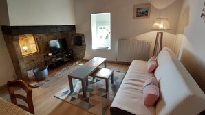 Una sala de estar con chimenea de piedra, un sofá, un televisor y una lámpara.