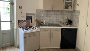 Cocina compacta con estufa a gas, pileta y lavavajillas, bajos de madera clara y un salpicadero de azulejos.