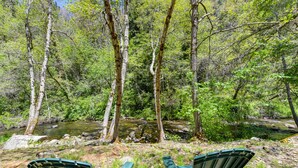 Two green Adirondack chairs facing a forested area with a stream. - Lux, creekfront 8-acre retreat with hot tub (Nevada City)