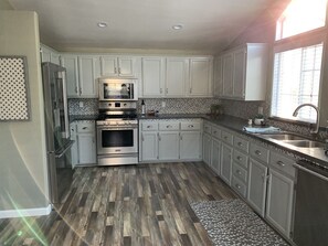 A kitchen with white cabinets, stainless steel appliances, a patterned backsplash, and a window providing natural light.