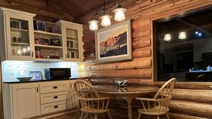 Une cuisine chaleureuse, aménagée dans le style d’un chalet, avec des murs en bois, un coin repas doté de deux chaises en bois et une grande fenêtre.