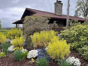 A rustic cabin with a stone chimney, surrounded by a garden with various flowering plants. - Log Home on 9 acres (Chehalis)